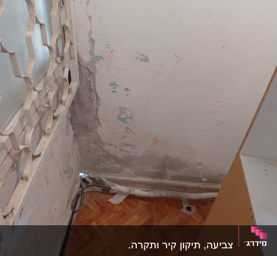קיר מתקלף עם סימני רטיבות ליד חלון עם סורגים